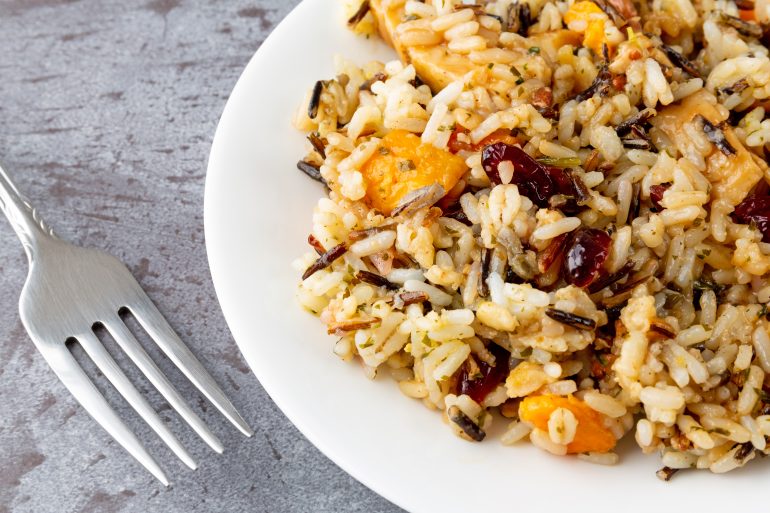 Chicken with pecans and wild rice on a plate with a fork to the side on a gray background