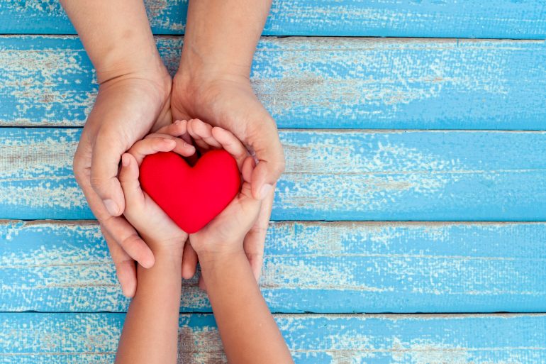 Red heart in child kid and mother hands on old blue wooden table