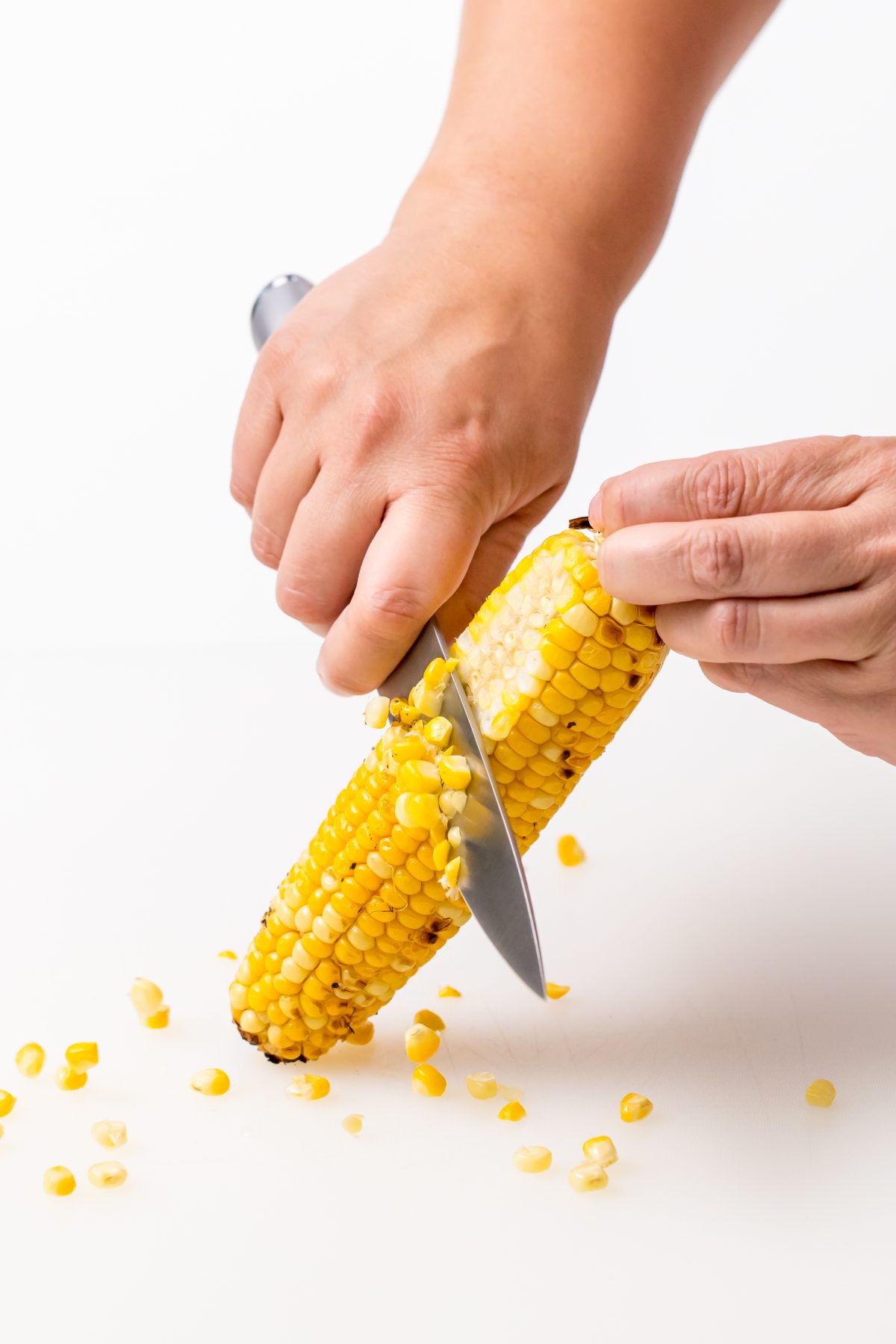 Remove corn from cob with knife for Grilled vegetable salad with Vidalia onion dressing