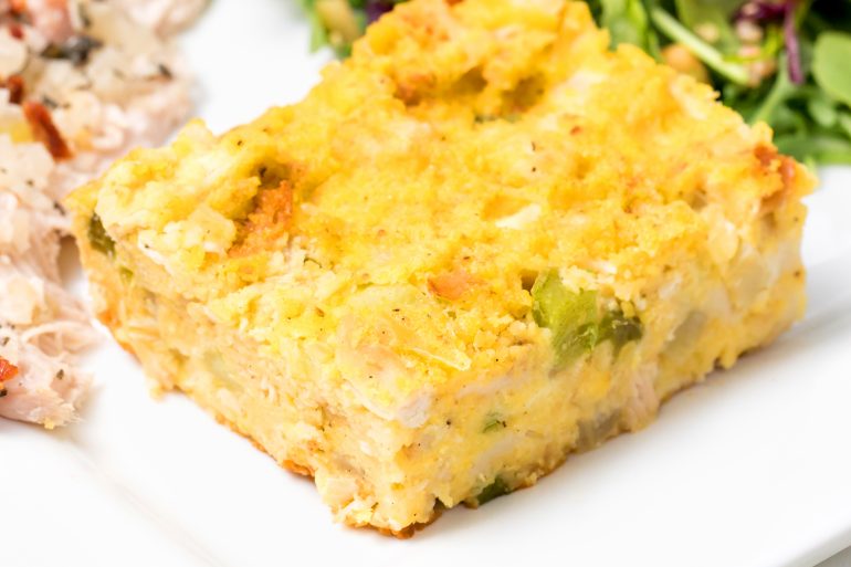 5D4B9924 - Homemade Southern Cornbread Dressing recipe - a plated dish of baked cornbread on a white table surrounded by celery, eggs, onion, bell pepper, corn and sage