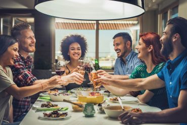 Group of happy friends toasting while eating at dining table.