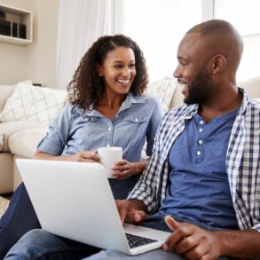 Young black couple using laptop at home look at each other