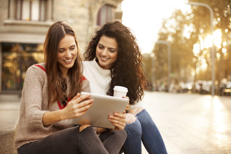 Two girl friends laughing at tablet outdoors street