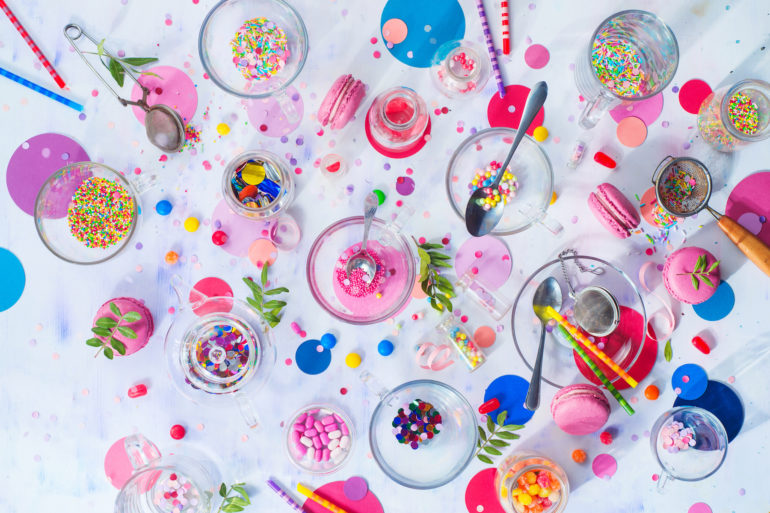 Party supplies in glass tea cups. Sprinkles, confetti, candies, macaroons and birthday candles on a white background. After party concept