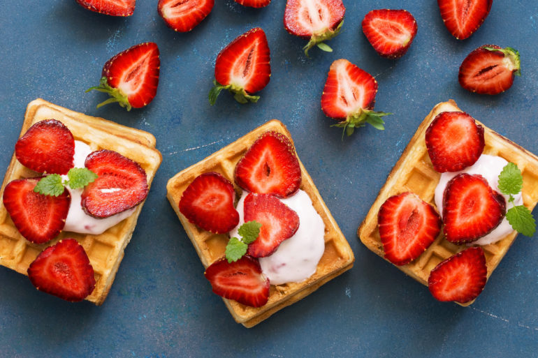 Homemade Belgian waffles with cream and fresh strawberries on a blue woody background. Top view, flat lay, space for text.