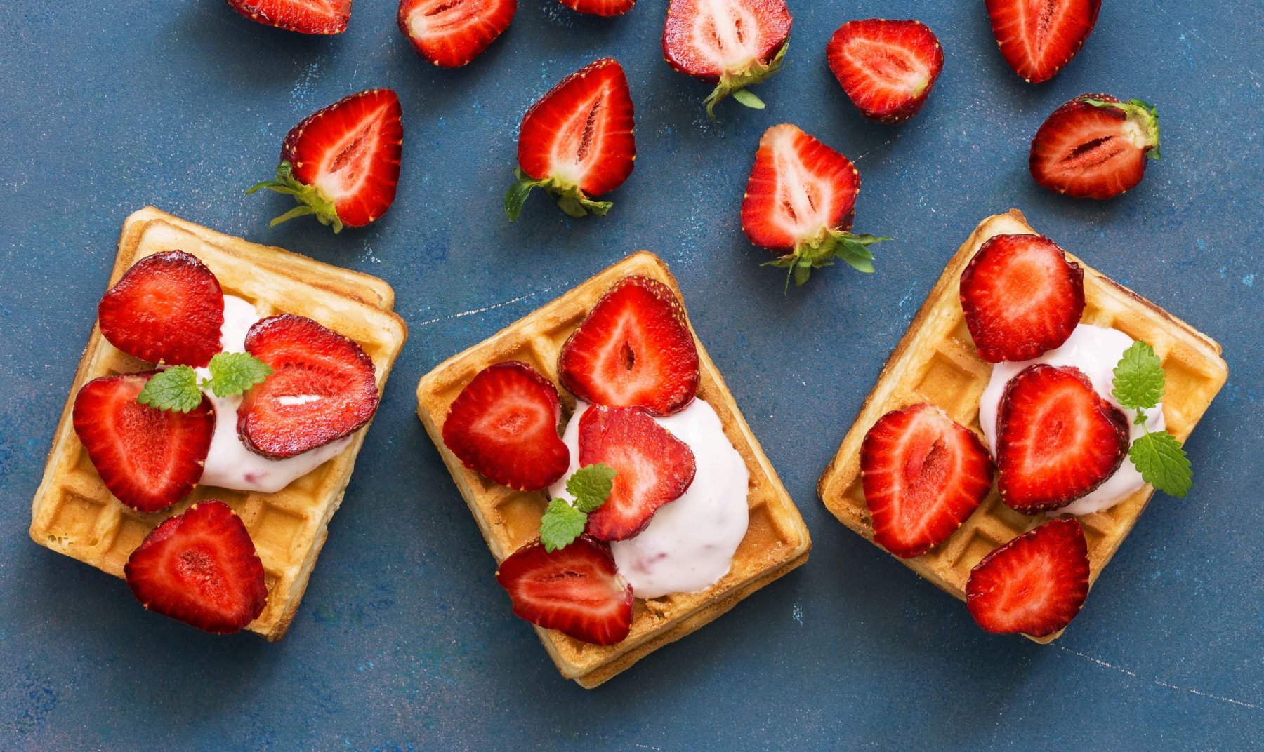 Homemade Belgian waffles with cream and fresh strawberries on a blue woody background. Top view, flat lay, space for text.