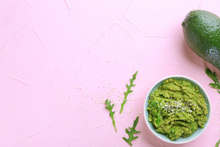 Bowl with tasty guacamole and ripe avocado on color background
