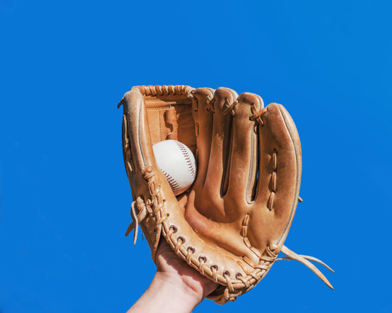 Hand in glove for a baseball game caught a leather white ball on a blue sky background. Sports contests. Victory. Achievement of success.