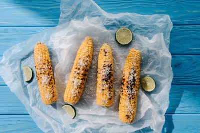 elevated view of grilled salted corn with lime slices on baking paper on wooden table