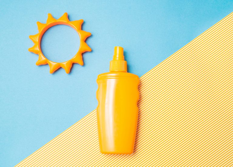 Bottle of sunscreen cream or lotion with sun toy flat lay on the blue and yellow background with copy space. Spf summer skin, uv protect top view