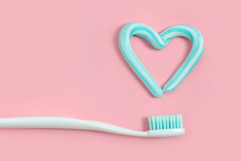 Toothbrushes and turquoise color toothpaste in shape of heart on pink background. Dental and healthcare concept.